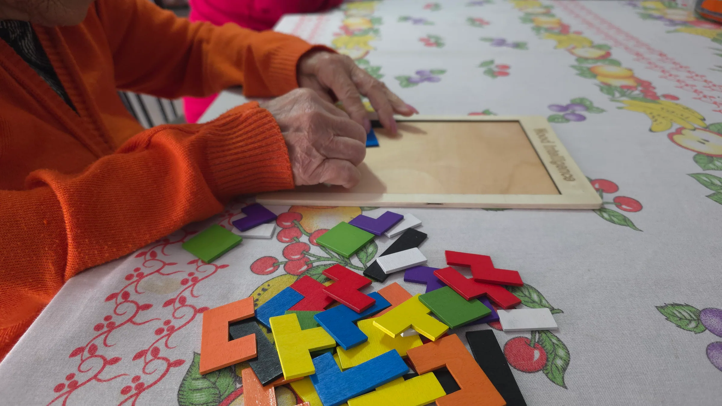 Mãos de uma pessoa idosa montando peças coloridas durante uma atividade acompanhada em casa.